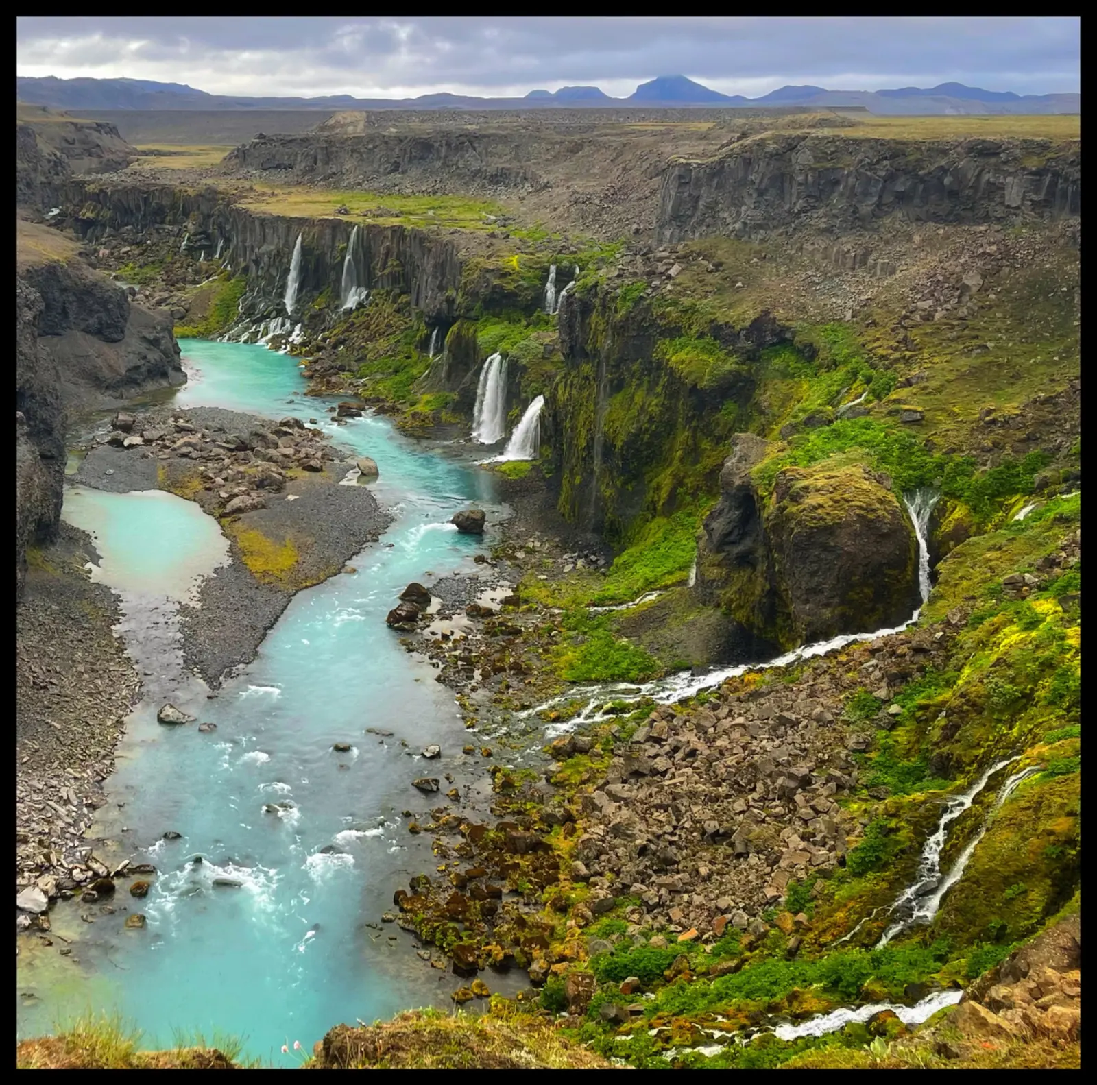 Turquoise river and waterfalls cutting through a rugged Icelandic canyon.
