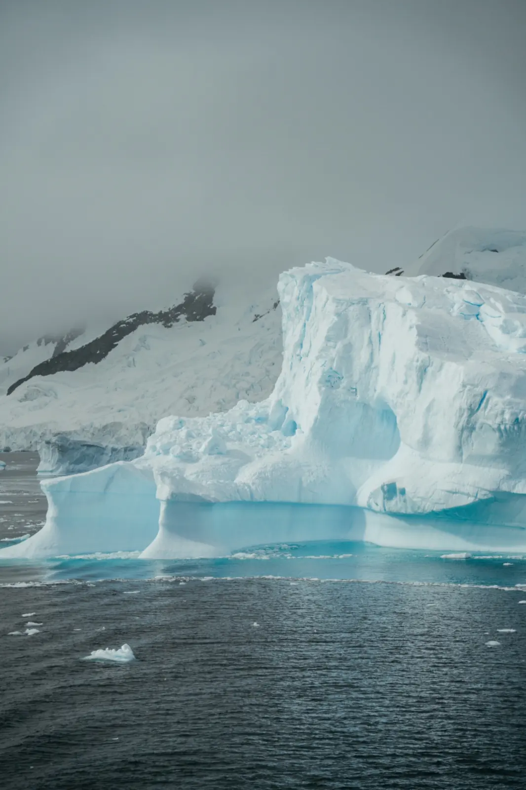 Blue glacier wall beneath dark mountain slopes.