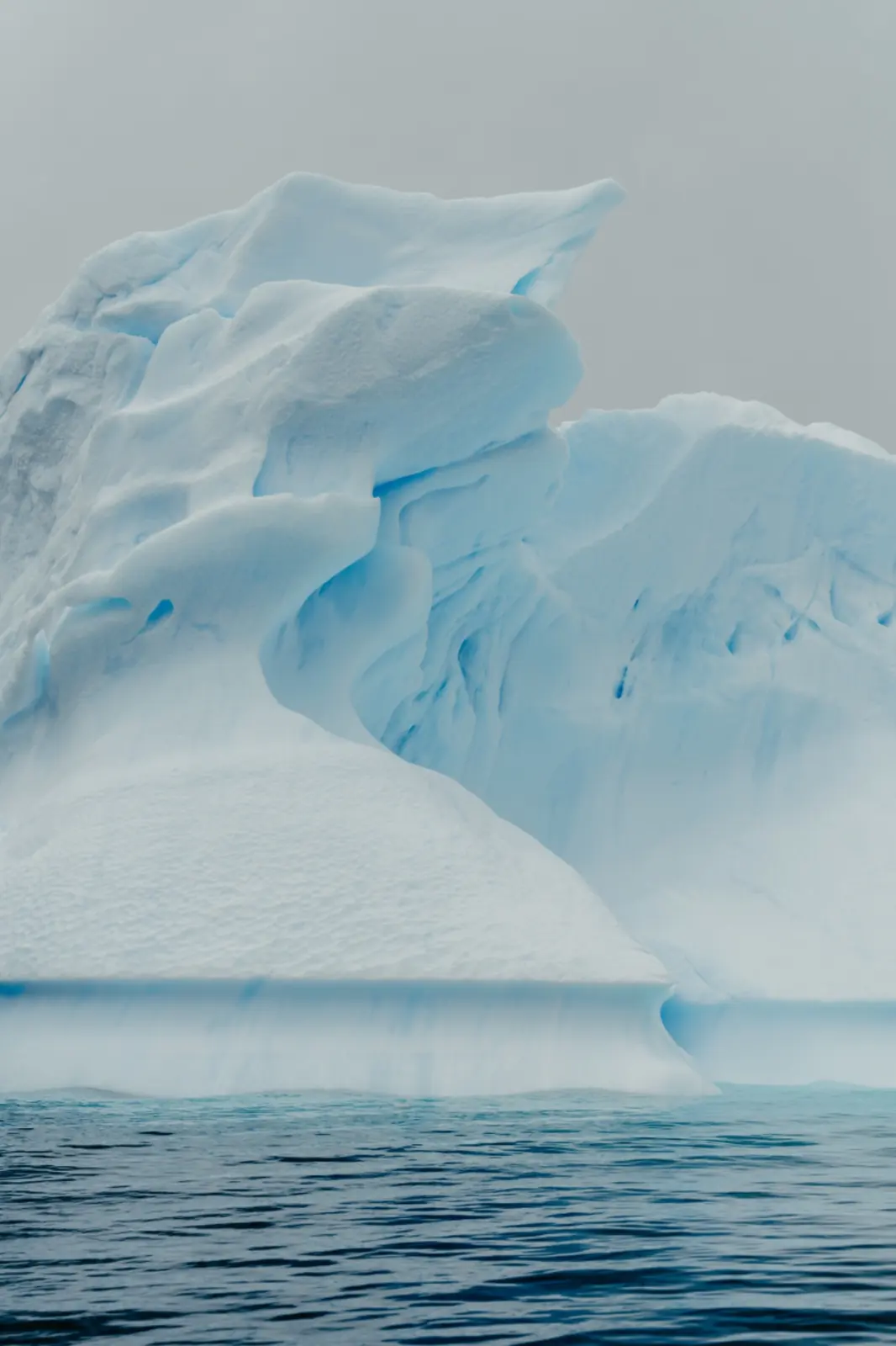 Sculpted blue-white iceberg above calm polar water.