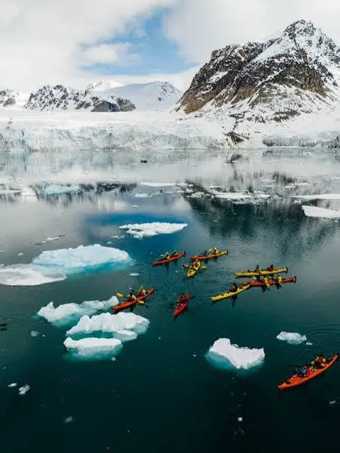 Kayakers weaving between floating ice beneath a mountain glacier.