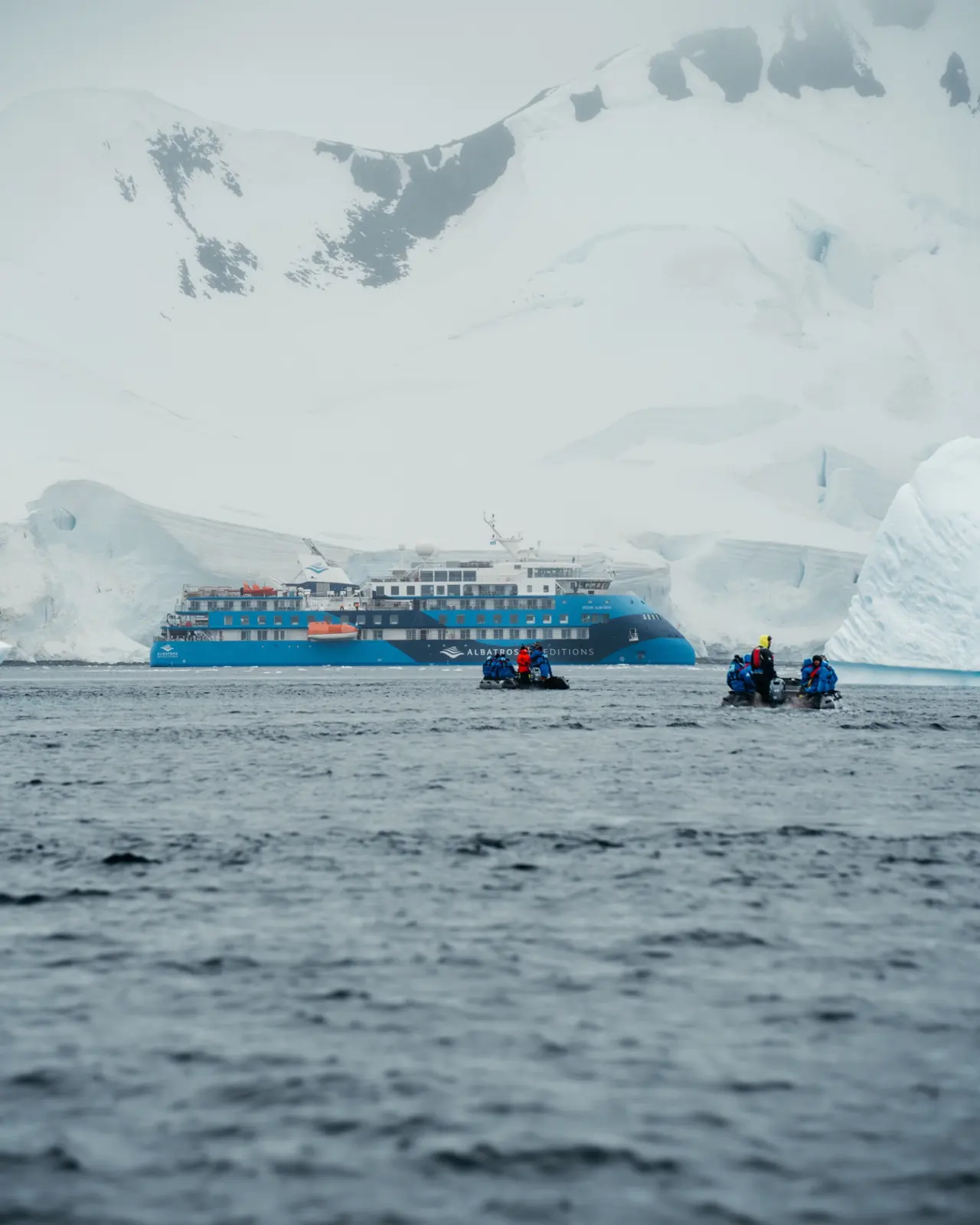 Expedition ship and zodiac boats beneath Antarctic glaciers.