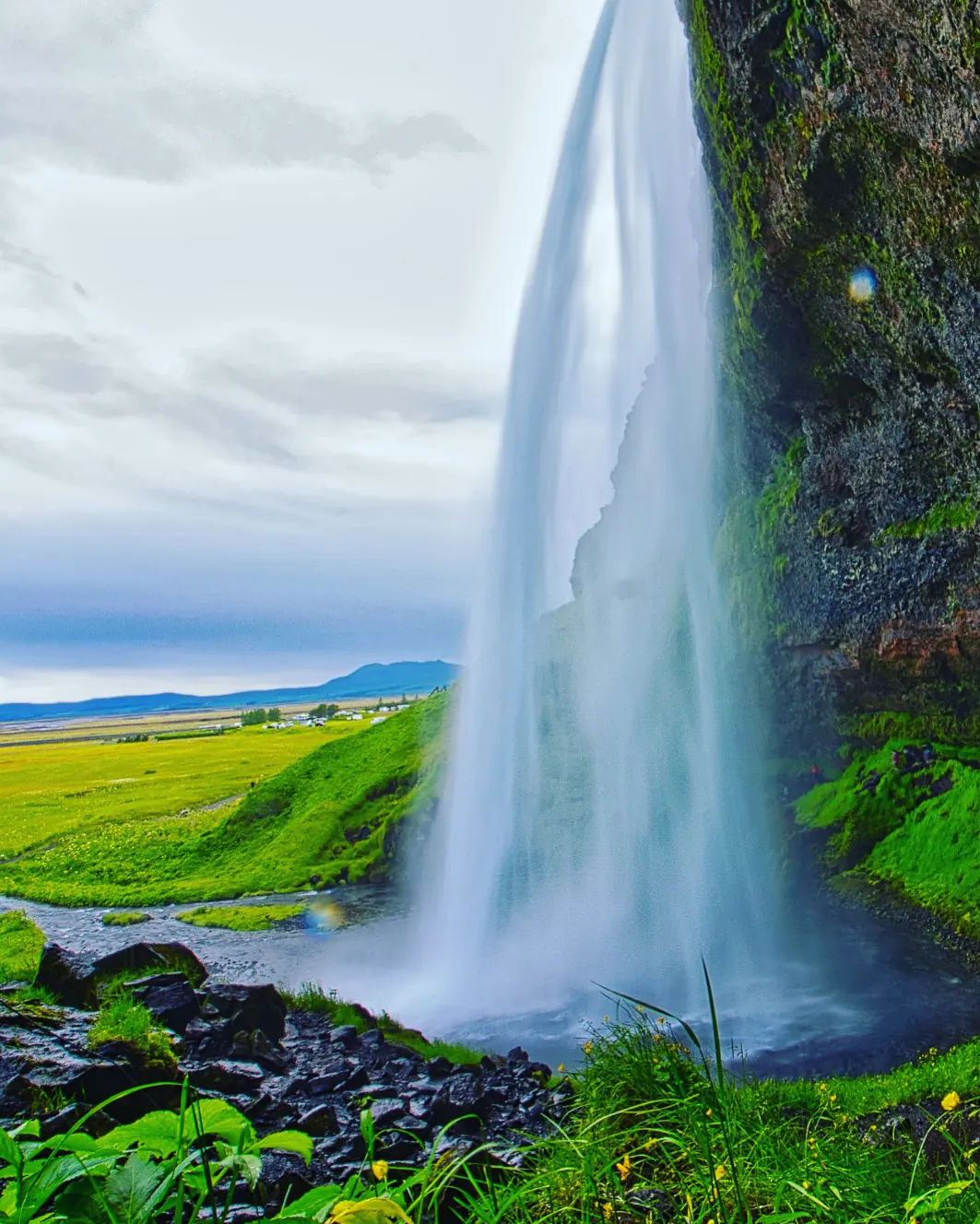 Waterfall cascading over a green Icelandic cliff.