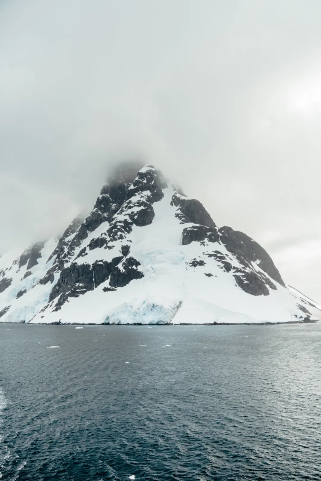 Snow-covered polar mountain disappearing into low cloud.