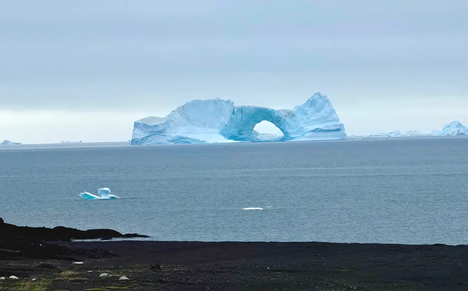 Natural arch formed in a large blue iceberg.