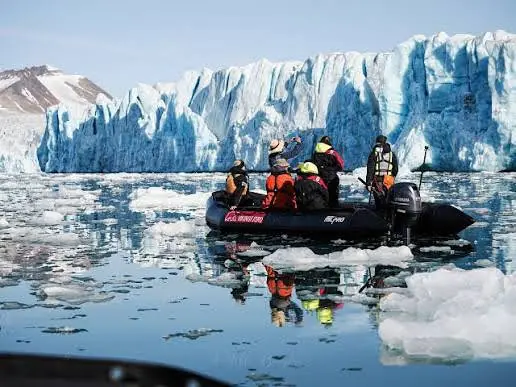 Zodiac expedition boat moving through broken ice beside a glacier.