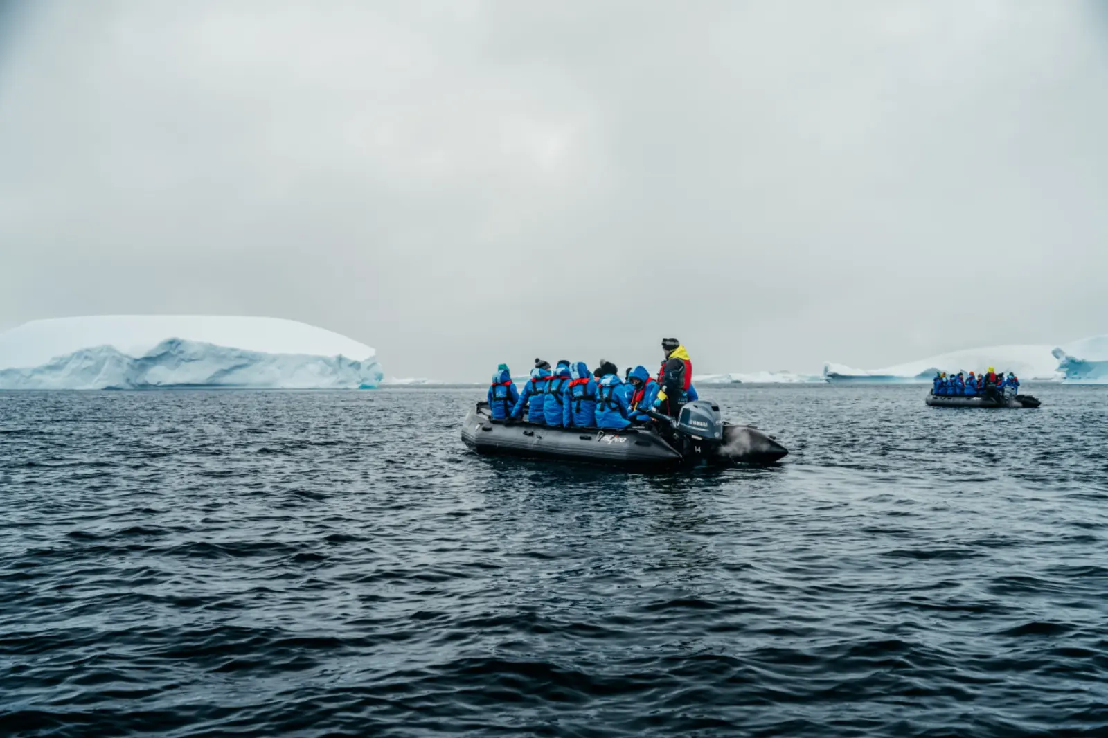 Two zodiac groups navigating Antarctic waters between icebergs.