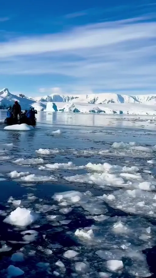 Zodiac boat crossing ice-filled Antarctic water beneath snow-covered peaks