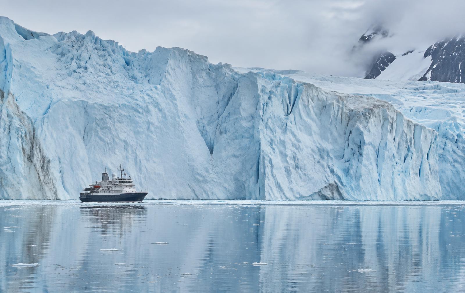 An ice-class expedition ship beneath an immense glacier wall